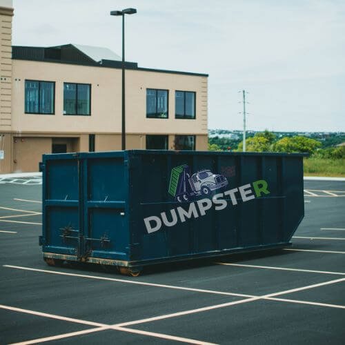 A dumpster placed in a parking lot, with cars parked around it and a concrete surface beneath.